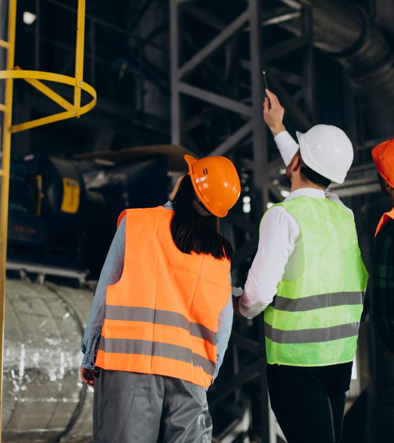 Three factory workers in safety hats discussing manufacture plan